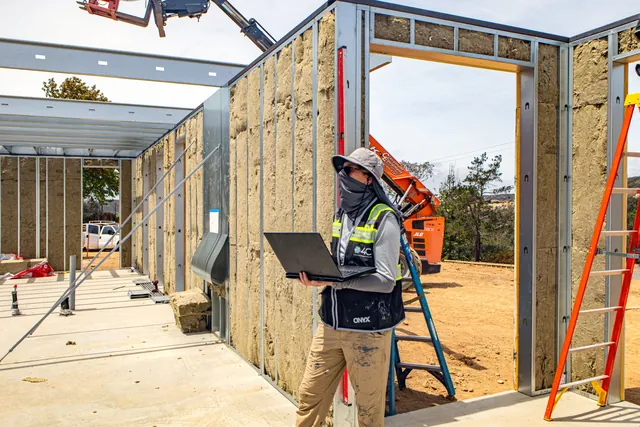 4C team member checking installed wall panels against the digital model on a laptop inside the Escondido Residence frame
