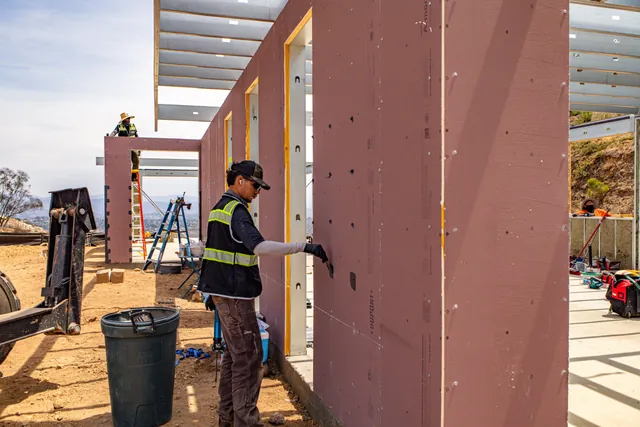 4C crew member sealing the exterior face of the wall panels at the Escondido Residence, with roof framing overhead