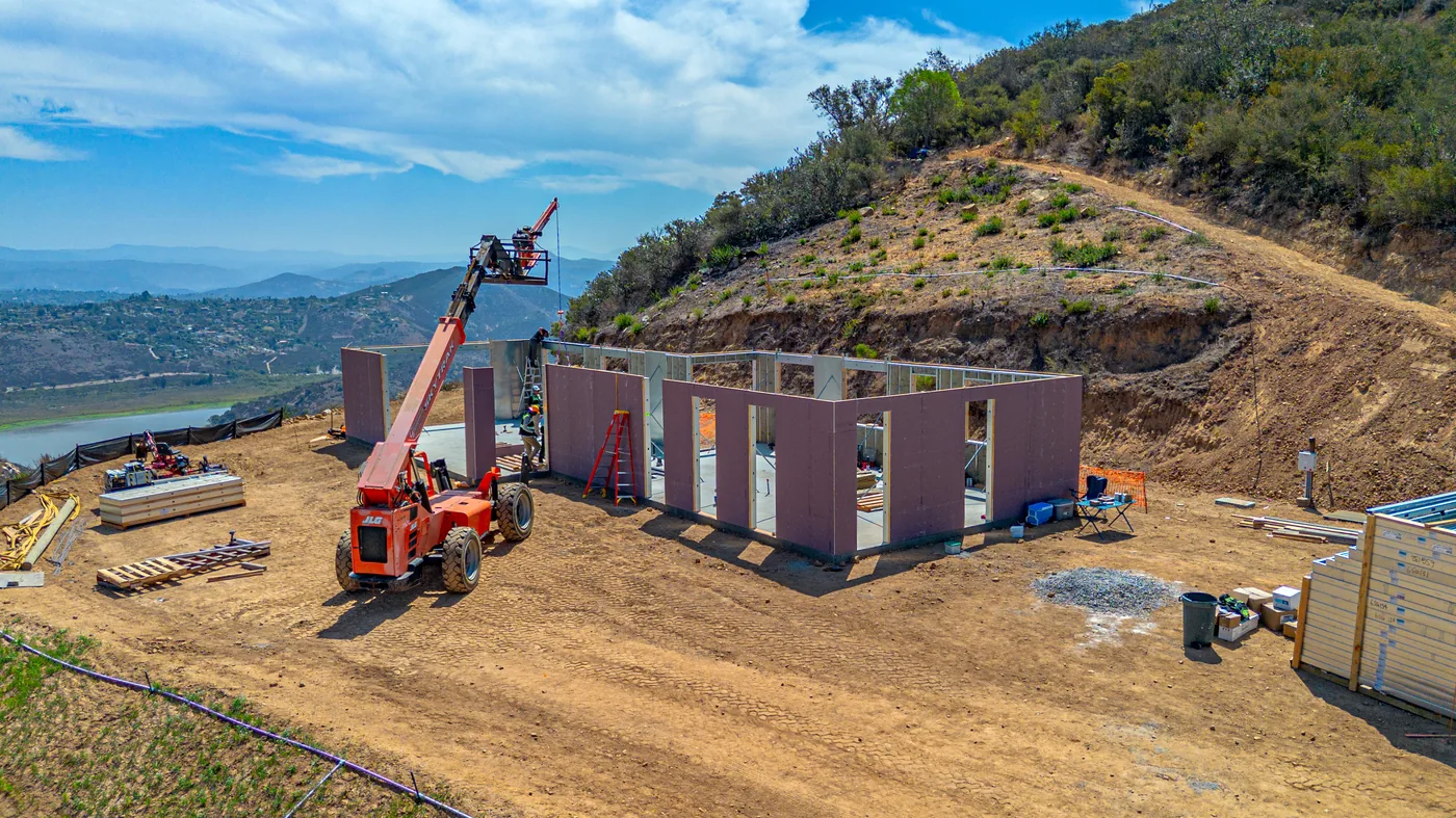 Telehandler lifting a SAFE wall panel into place at the Escondido Residence, framing underway with the reservoir in the background